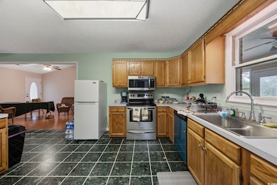 Kitchen featuring stainless steel appliances, a sink, light countertops, brown cabinetry, and a textured ceiling