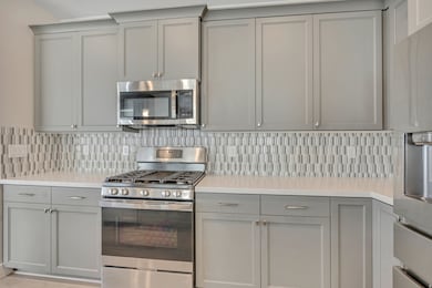 Kitchen featuring gray cabinets, appliances with stainless steel finishes, backsplash, and light stone countertops