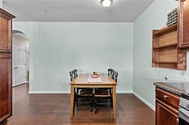 Dining area with arched walkways and dark wood-type flooring