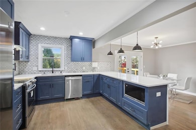 Kitchen with an inviting chandelier, hardwood / wood-style floors, hanging light fixtures, kitchen peninsula, and stainless steel appliances