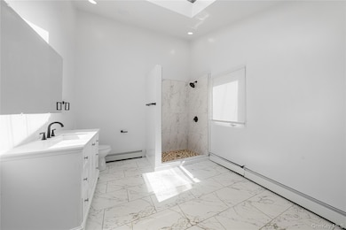 Bathroom with a baseboard radiator, a tile shower, vanity, marble finish floors, and recessed lighting