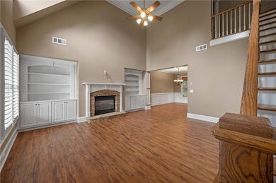 Unfurnished living room featuring a high ceiling, a fireplace, a ceiling fan, wood finished floors, and a chandelier