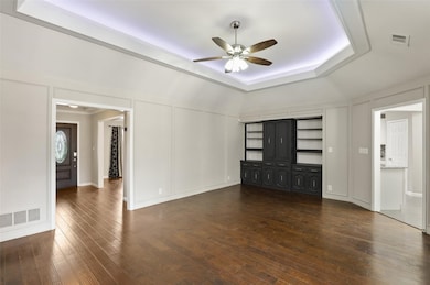 Unfurnished living room featuring a decorative wall, dark wood-style flooring, ceiling fan, and a raised ceiling