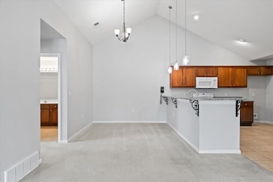 Dining to kitchen with white microwave, high vaulted ceiling, light countertops, light colored carpet, and hanging light fixtures
