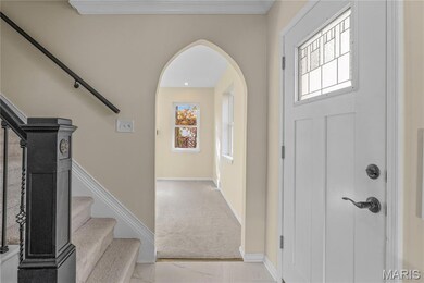 Foyer entrance featuring arched walkways, stairs, light colored carpet, and light marble finish floors