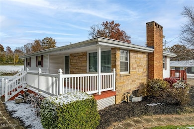 View of snow covered exterior featuring stone siding, a wooden deck, and a chimney