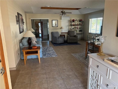Living room with a textured wall, a textured ceiling, light tile patterned flooring, and a ceiling fan
