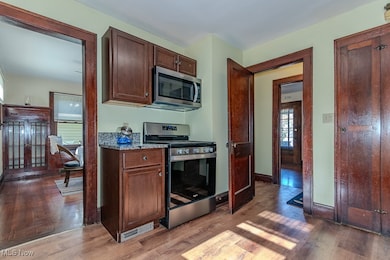 Kitchen with stainless steel appliances, light wood-style floors, light stone counters, and dark brown cabinetry