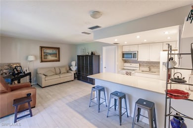 Kitchen featuring kitchen peninsula, white appliances, sink, white cabinetry, and a breakfast bar area
