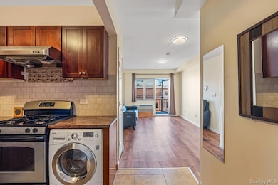 Kitchen featuring gas range, washer / clothes dryer, decorative backsplash, ventilation hood, and light tile patterned floors