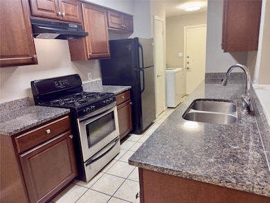 Kitchen featuring stainless steel range with gas stovetop, light tile patterned floors, under cabinet range hood, dark stone counters, and independent washer and dryer