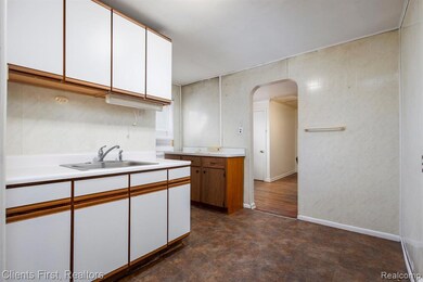 Kitchen featuring brown cabinets, white cabinetry, arched walkways, and light countertops