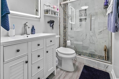 Bathroom with a marble finish shower, vanity, and light wood-style floors