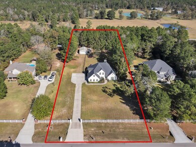 This aerial view showcases a spacious property with a charming house surrounded by lush greenery. The long driveway leads to the residence, which is set back from the road, providing privacy. The lot includes a mix of open lawn and mature trees, offering a serene, natural setting.