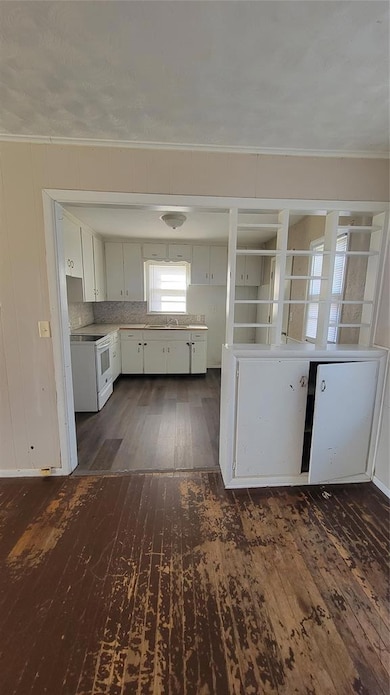 Kitchen with dark wood-style floors, white cabinets, light countertops, range, and crown molding