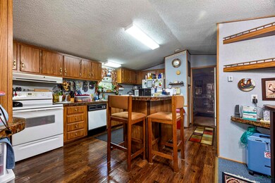 Kitchen with white appliances, a breakfast bar area, dark countertops, dark wood-style floors, and brown cabinetry