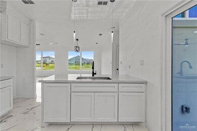 Kitchen featuring pendant lighting, light stone counters, light tile floors, sink, and white cabinetry