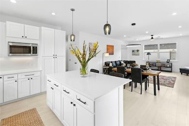 Kitchen with stainless steel microwave, open floor plan, a ceiling fan, recessed lighting, and white cabinetry