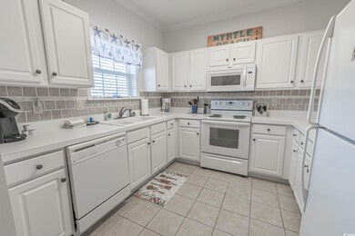 Kitchen with white appliances, a sink, tasteful backsplash, white cabinetry, and ornamental molding