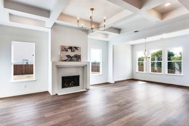Unfurnished living room with a chandelier, coffered ceiling, beam ceiling, wood finished floors, and a brick fireplace