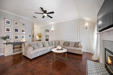 Living room featuring a fireplace, arched walkways, dark wood-type flooring, crown molding, and ceiling fan