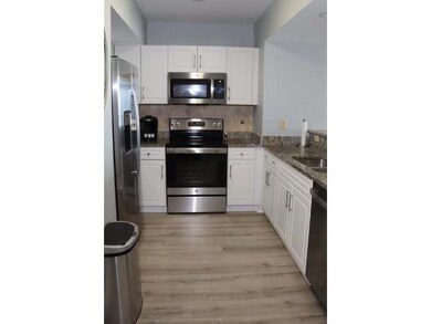Kitchen featuring stainless steel appliances, white cabinetry, decorative backsplash, light wood-type flooring, and dark stone countertops