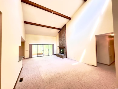 Unfurnished living room featuring high vaulted ceiling, carpet, beamed ceiling, and a brick fireplace