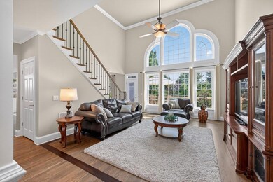 Living room featuring stairs, ceiling fan, ornamental molding, wood finished floors, and a towering ceiling