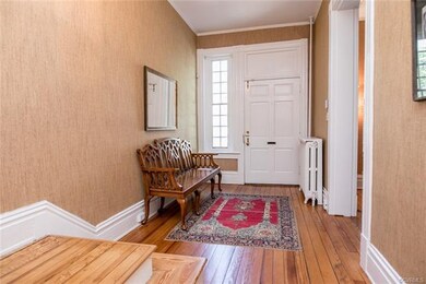 Front door has glass pane sidelight, grass cloth wall covering, hardwood floors, and crown molding.