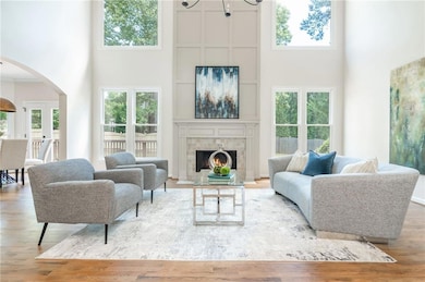 Living room with a towering ceiling, arched walkways, wood finished floors, a fireplace, and a chandelier