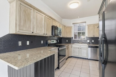 Kitchen with black appliances, light tile patterned floors, decorative backsplash, light stone counters, and crown molding