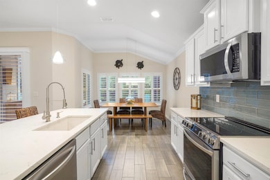 Kitchen featuring appliances with stainless steel finishes, ornamental molding, white cabinets, decorative backsplash, and hanging light fixtures