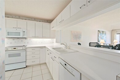 Kitchen with white appliances, a textured ceiling, light countertops, light tile patterned flooring, and white cabinetry