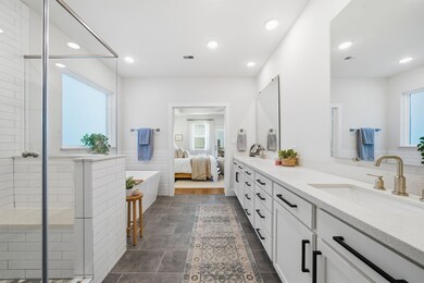 Primary bath features a free standing soaker tub and a shower with bench. A long stretch of counter space and two sinks lead to the linen shelves and walk-in closet.