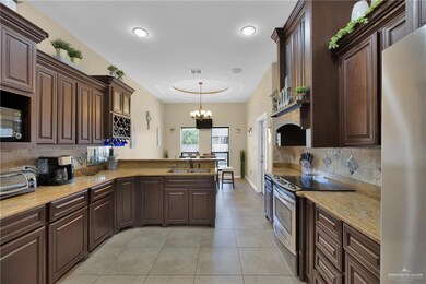 Kitchen featuring appliances with stainless steel finishes, a peninsula, light tile patterned flooring, backsplash, and a chandelier