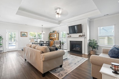 Living room with a tray ceiling, dark wood-type flooring, crown molding, and a chandelier