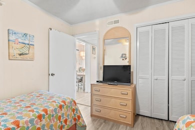 Bedroom with light wood-type flooring, ornamental molding, a closet, and visible vents