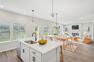 Kitchen with stainless steel dishwasher, light wood-style floors, a glass covered fireplace, an island with sink, and white cabinets