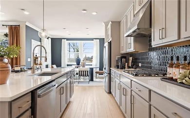Kitchen featuring pendant lighting, stainless steel appliances, light countertops, a sink, and under cabinet range hood