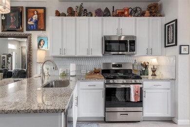 Kitchen with stainless steel appliances, a peninsula, light stone counters, backsplash, and white cabinets