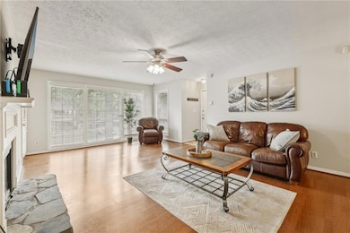 Living area with ceiling fan, a fireplace with raised hearth, baseboards, wood finished floors, and a textured ceiling