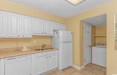 Kitchen featuring washer / dryer, white appliances, white cabinets, light tile patterned floors, and a textured ceiling