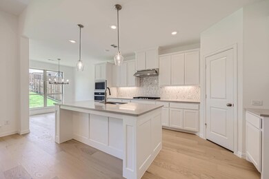 Kitchen with tasteful backsplash, white cabinets, a center island with sink, light hardwood / wood-style floors, and decorative light fixtures