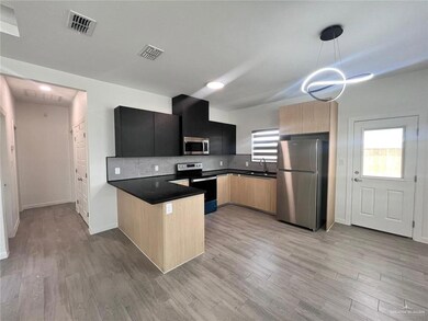 Kitchen with light brown cabinets, light wood-type flooring, stainless steel appliances, and hanging light fixtures