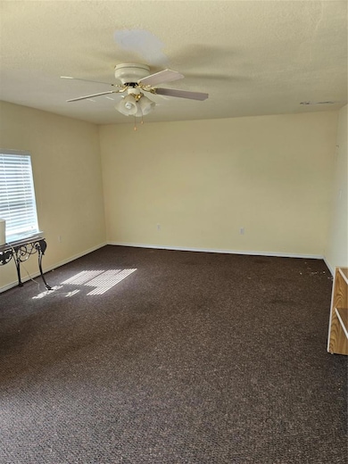 Unfurnished room featuring dark carpet, a textured ceiling, and a ceiling fan