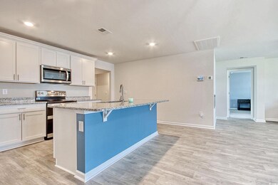 Kitchen featuring stainless steel appliances, a center island with sink, light wood finished floors, white cabinetry, and light stone countertops