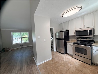 Kitchen featuring stainless steel appliances, a textured ceiling, light wood finished floors, light stone countertops, and white cabinets