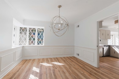 Unfurnished dining area with crown molding, light wood finished floors, a chandelier, a decorative wall, and a wainscoted wall