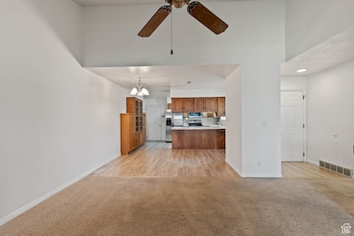 Kitchen featuring appliances with stainless steel finishes, light carpet, ceiling fan, brown cabinetry, and a peninsula
