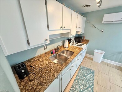 Kitchen with a sink, a wall mounted AC, black microwave, white cabinetry, and stovetop